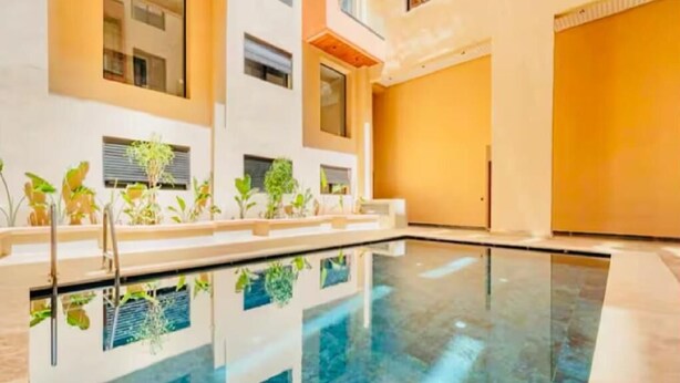 Una piscina interior moderna con paredes de vidrio transparente, rodeada de plantas en macetas y un diseño limpio y minimalista.