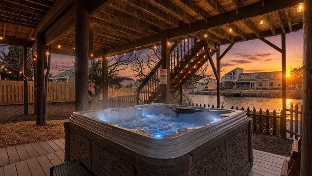 A hot tub under a wooden pergola with a view of a river and houses.