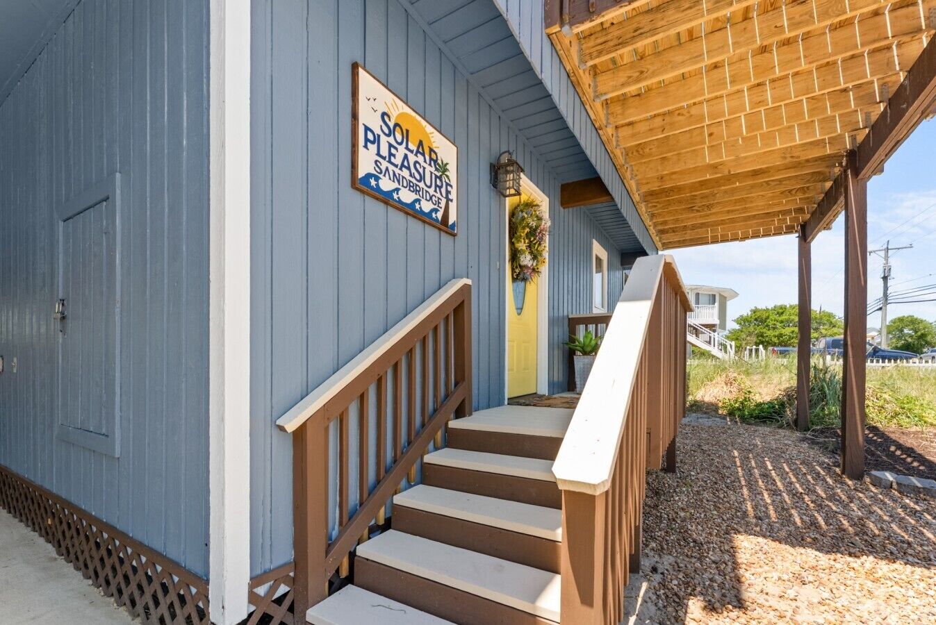 Eine Holztreppe führt zu einer Veranda mit einem Schild, auf dem 'Solar Pleasure Sandbridge' steht.