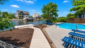 A backyard with a swimming pool, a dock, and houses in the background.