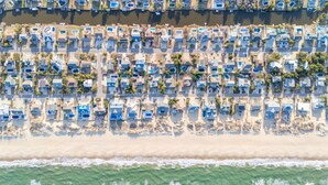 An aerial view of a coastal resort with rows of beachside villas, each with a private pool and direct beach access.