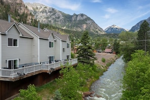 Ein Haus mit einer Terrasse, das auf einen Fluss mit Blick auf Berge blickt.