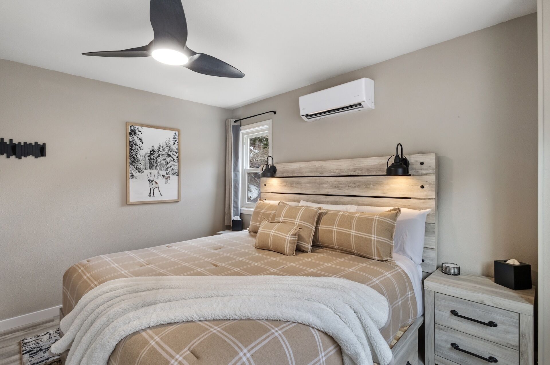 Une chambre à coucher comprenant un lit, des tables de chevet, un ventilateur de plafond, un climatiseur et un tableau encadré accroché au mur.