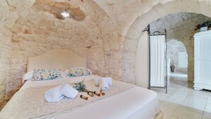 Ein Schlafzimmer mit Stehwänden, einem Bett mit floralen Kissen, einem weißen Kopfteil und einer weißen Tür im Hintergrund.