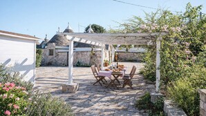 Ein Steinhaus mit weißem Dach und einer Pergola, auf der ein Tisch und Stühle stehen.