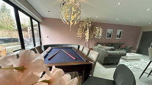 A modern living room with a pool table, a sofa, and a chandelier. - Luxury 5-Bed Hale Home | Cinema, Pool Table & Sleeps 10 (Hale Barns)