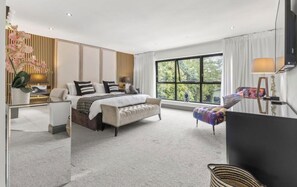 A modern bedroom with a large bed, a sitting area, and a window with a view.