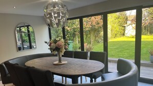 A modern dining area with a round table, black chairs, and a decorative light fixture. - Luxury 5-Bed Hale Home | Cinema, Pool Table & Sleeps 10 (Hale Barns)