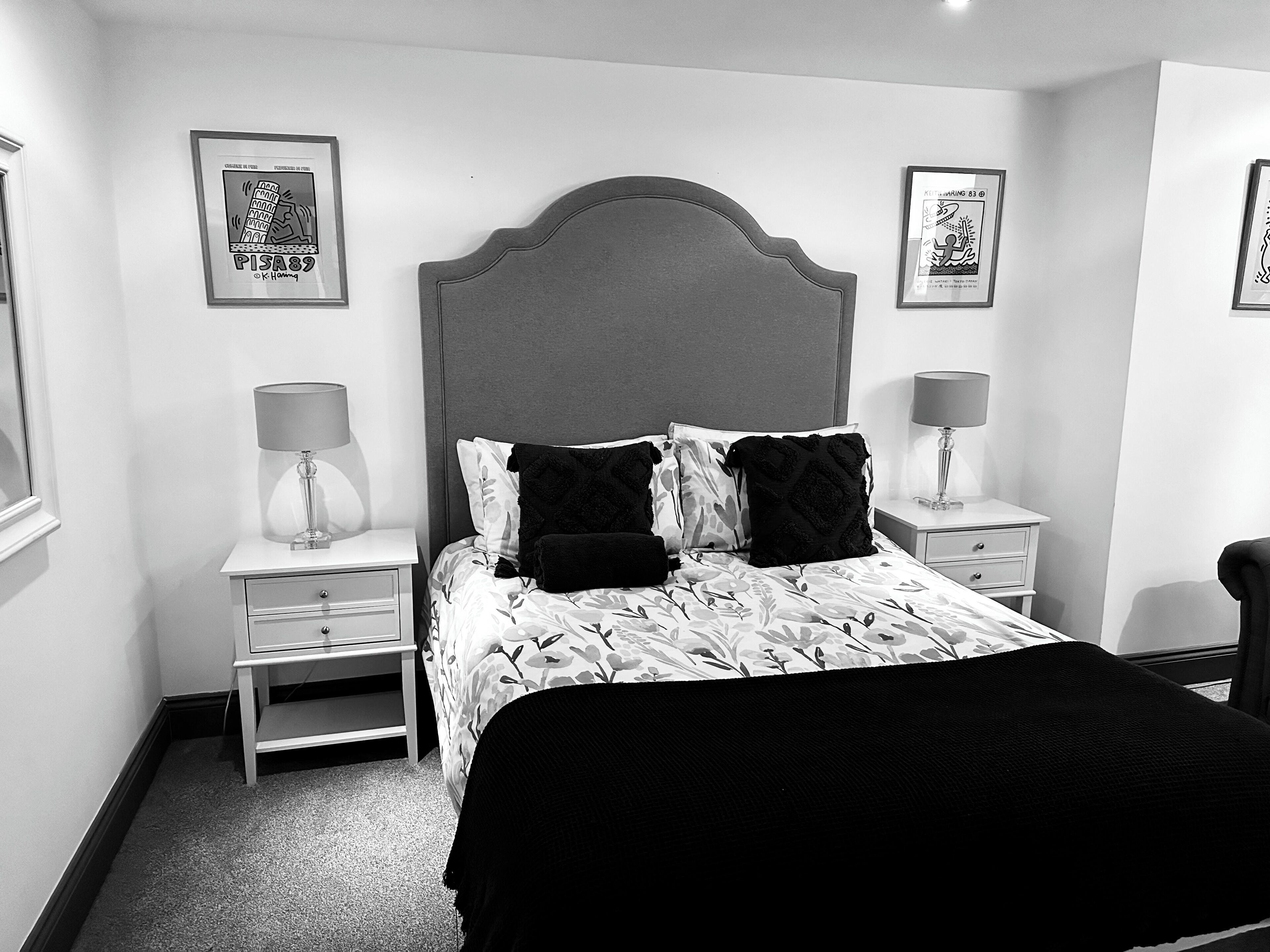 Une chambre à coucher avec un grand lit, deux tables de chevet avec des lampes, un fauteuil et des œuvres d’art encadrées accrochées aux murs.