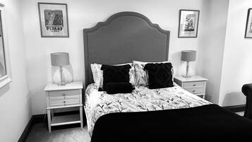 Une chambre à coucher avec un grand lit, deux tables de chevet avec des lampes, un fauteuil et des œuvres d’art encadrées accrochées aux murs.