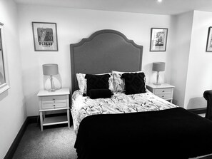 Un dormitorio con una cama grande, dos mesitas de noche con lámparas, una silla y cuadros en las paredes.