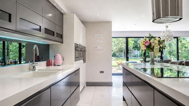 A modern kitchen with sleek cabinetry, a stainless steel range hood, and a large window offering a view of the outdoors. - Luxury 5-Bed Hale Home | Cinema, Pool Table & Sleeps 10 (Hale Barns)