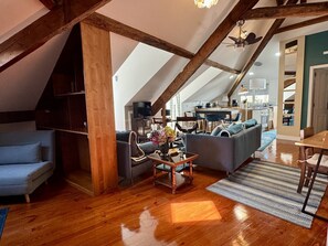 A loft-style living space with exposed wooden beams, a sofa, a coffee table, and a kitchen area in the background. - Feel simply blue and amazed (Lisboa)