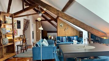 Un espacio tipo loft con vigas de madera a la vista, un sofá azul, una mesa de comedor y una lámpara de pie.