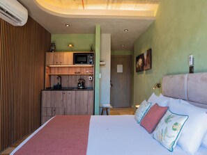A compact hotel room with a kitchenette, a bed with multiple pillows, and a small table.