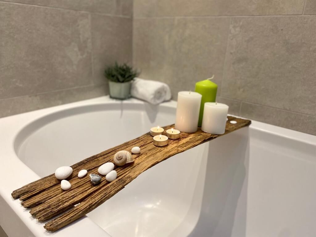Une salle de bain avec une étagère en bois sur laquelle sont posées des bougies et des pierres.