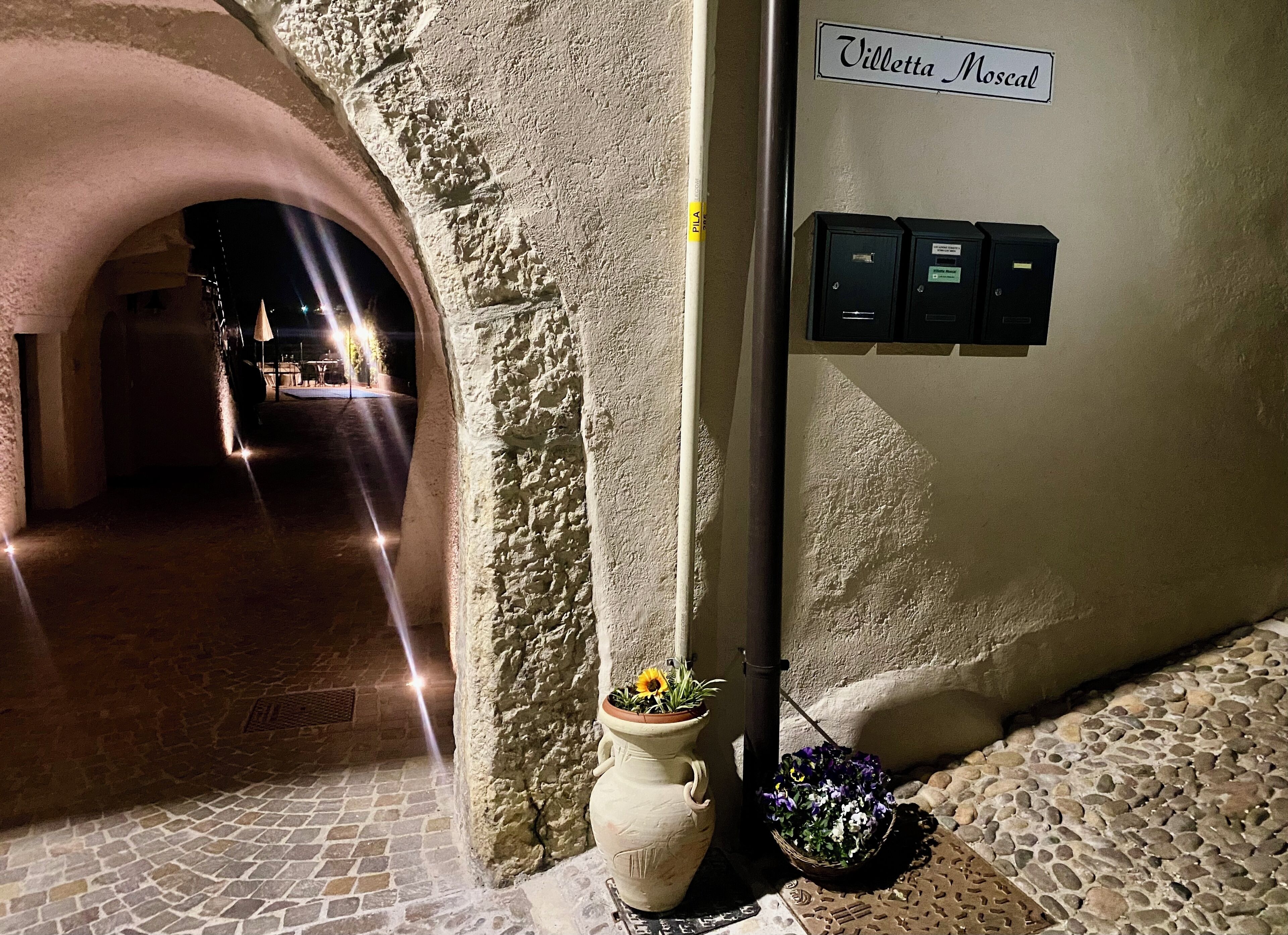 Un carrer estret amb paviment de pedra, una paret blanca amb un rètol que diu "Villette Moscal" i un pal de llum amb caixes elèctriques.