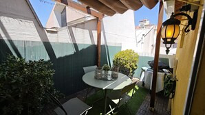 Een klein terras buiten met een ronde tafel, stoelen, een bloempot en een hanglamp.