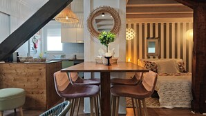 Een eethoek met een houten tafel, twee stoelen, een potplant en een spiegel aan de muur.