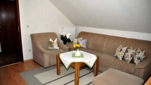 Una sala de estar con un sofá marrón, una mesa de centro de madera con un jarrón de flores y un cojín estampado.