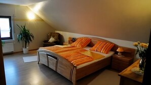 Un dormitorio con cama, mesitas de noche, una silla, una planta en maceta y una ventana.