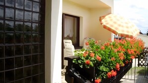 Un balcón con una maceta de flores, una silla blanca y un paraguas a cuadros.