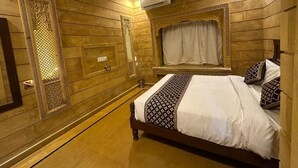 Een slaapkamer met een wandpaneel van hout, een bed met beddengoed met een patroon, een raam met gordijnen en een plafondventilator.