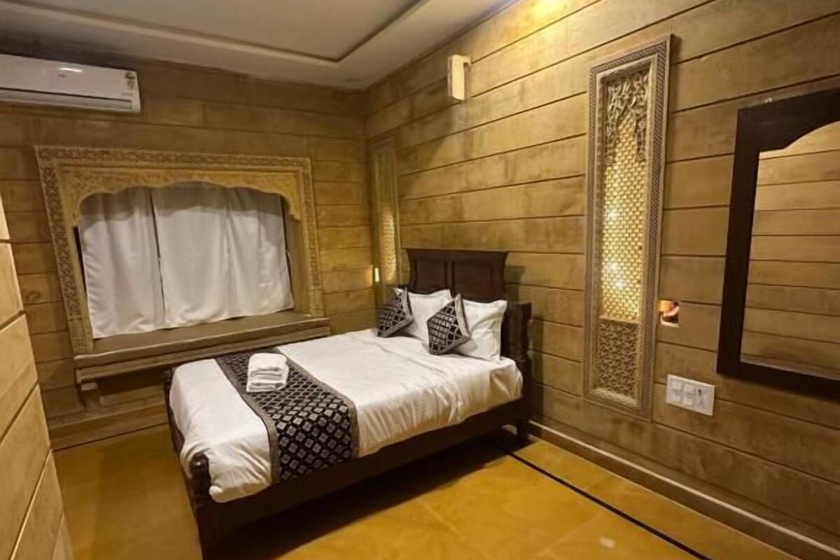 Une chambre à coucher comprenant un lit, un ventilateur de plafond, un appareil de climatisation, une fenêtre avec des rideaux et un miroir décoratif.