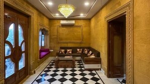 Een kamer met een zwart-wit schakeerd patroon op de vloer, een zithoek, een kroonluchter en een plafondventilator.