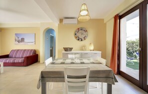 A dining area with a table set for two, a red sofa, a wall clock, and a view of the outdoors. - Cosy apartment for 4 guests with A/C, WIFI, TV and veranda (Punta Secca)
