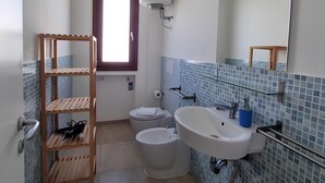 Une salle de bain avec une étagère en bois, deux toilettes, un lavabo et un grand miroir.