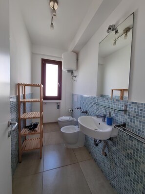 Ein Badezimmer mit Holzregal, zwei Toiletten, einem Waschbecken und einem großen Spiegel.