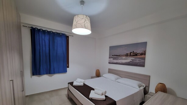 Une chambre à coucher bien rangée, avec un lit, un tableau, une lampe et une fenêtre avec des rideaux.