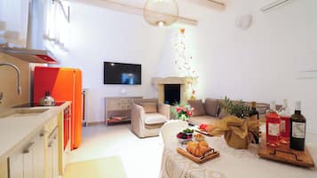 A living room with a sofa, a flat-screen TV, a fireplace, and a table with food and drinks.
