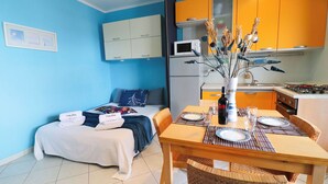 Een compacte kamer met een bed, een eettafel gedekt voor twee personen, een magnetron en een klein keukentje.