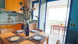 Een eethoek met een tafel gedekt voor vier personen, een keuken op de achtergrond en een balkon met een tafel en stoelen.
