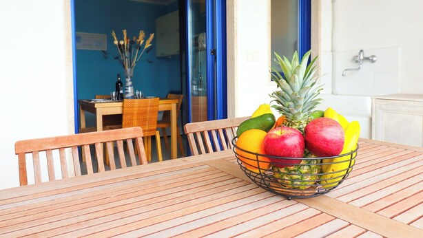 Een houten tafel met een fruitschaal met appels, bananen en een ananas.