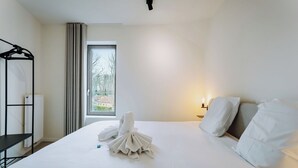 Una camera d'albergo con un letto rifatto, una finestra vista esterna, un comodino con una lampada e una rastrelliera in metallo nero.