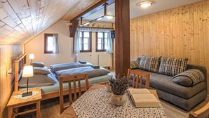 Ein gemütliches Zimmer mit schrägem Dach, Holzwänden, einer Couch, einem Bett, einem Tisch mit Buch und Vase sowie einem Fenster mit Vorhängen.