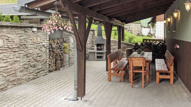 Eine Terrasse im Freien mit Steinmauern, einer Holz-Pergola und einem Grillbereich.