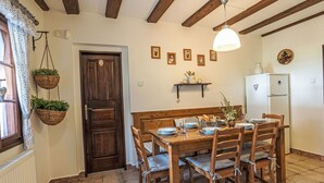 Ein Essbereich mit Holztisch und -stühlen, einer hängenden Pflanze, einem weißen Kühlschrank und einer Holztür.