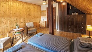 Ein gemütlicher Raum mit Holzwänden und -decke, einem Bett mit karierter Bettwäsche, einem Sessel, einem kleinen Tisch mit einer Vase und einer Lampe.
