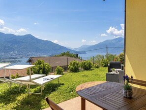 A patio with a table and chairs, a small garden, and a view of mountains and a lake. - Lovely apartment for 4 people with WIFI, TV, patio, pets allowed and panoramic view (Aurogna)