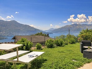 Eine Terrasse mit Tisch und Stühlen, ein kleines Gebäude und eine gebirgige Landschaft im Hintergrund.