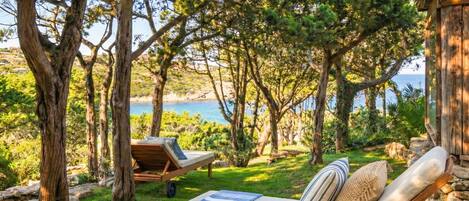 A serene outdoor seating area with wooden loungers and a stone wall, overlooking a coastal landscape.