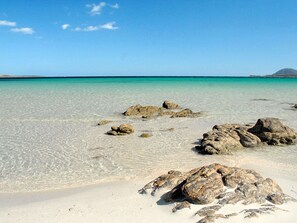 A beach with clear turquoise water, scattered rocks, and a distant island. - Cosy apartment for 6 people with A/C, pool, TV and pets allowed (Arzachena)