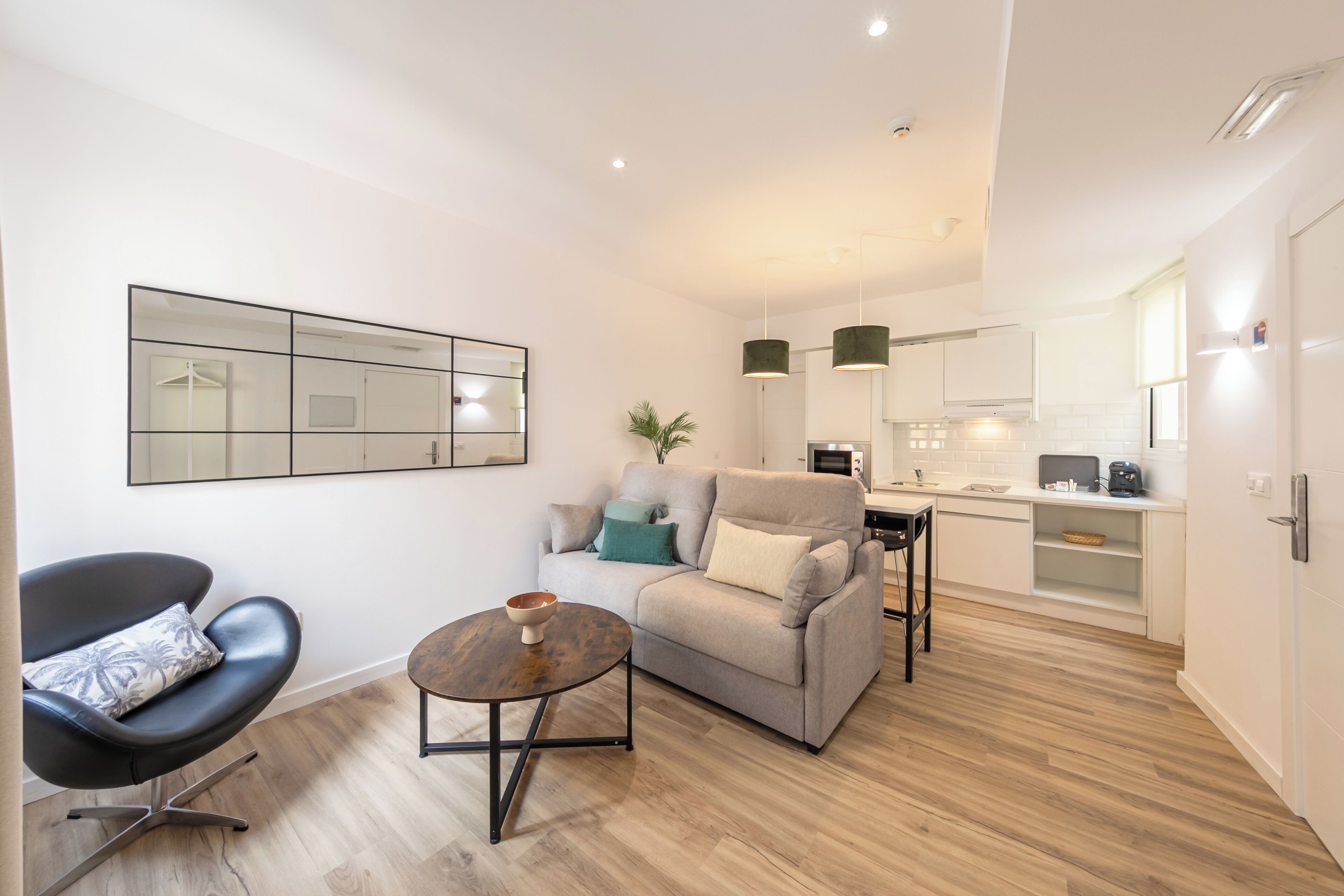A modern living room with a sofa, a coffee table, and a chair. There is a kitchen area with cabinets and a countertop.