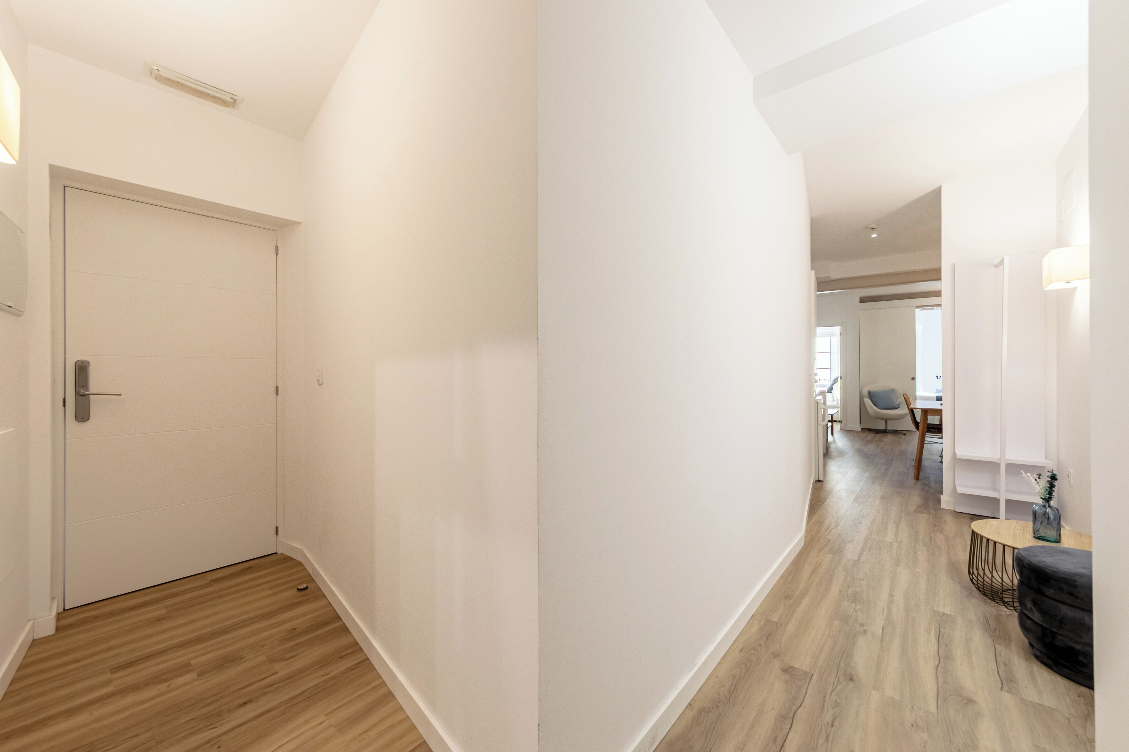 Un couloir avec un plancher en bois, des murs blancs et une porte.