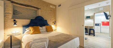 Un dormitorio con cama, lámparas de noche, cabecero y vista hacia una cocina.