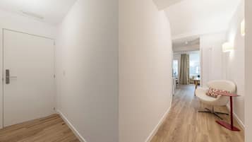 Um corredor com uma porta, uma cadeira com base vermelha e uma mesa com base vermelha.